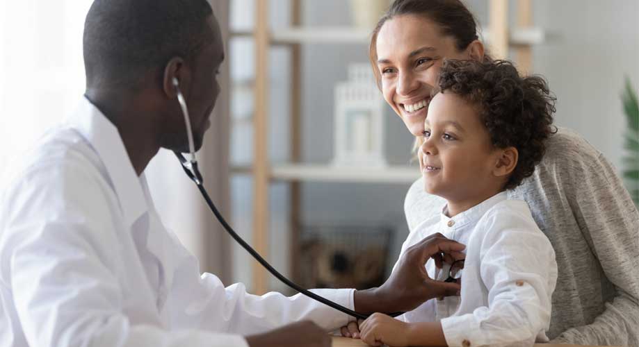 Pediatrician holding a stethoscope up to a child boy patient