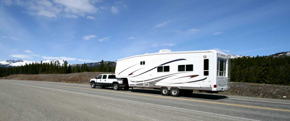 A white truck pulling a white trailer on a road with a mountain in front