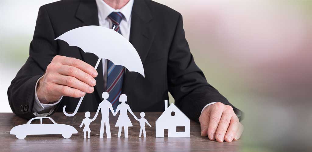 Man in a suit holding a paper umbrella over a paper family, car, and house
