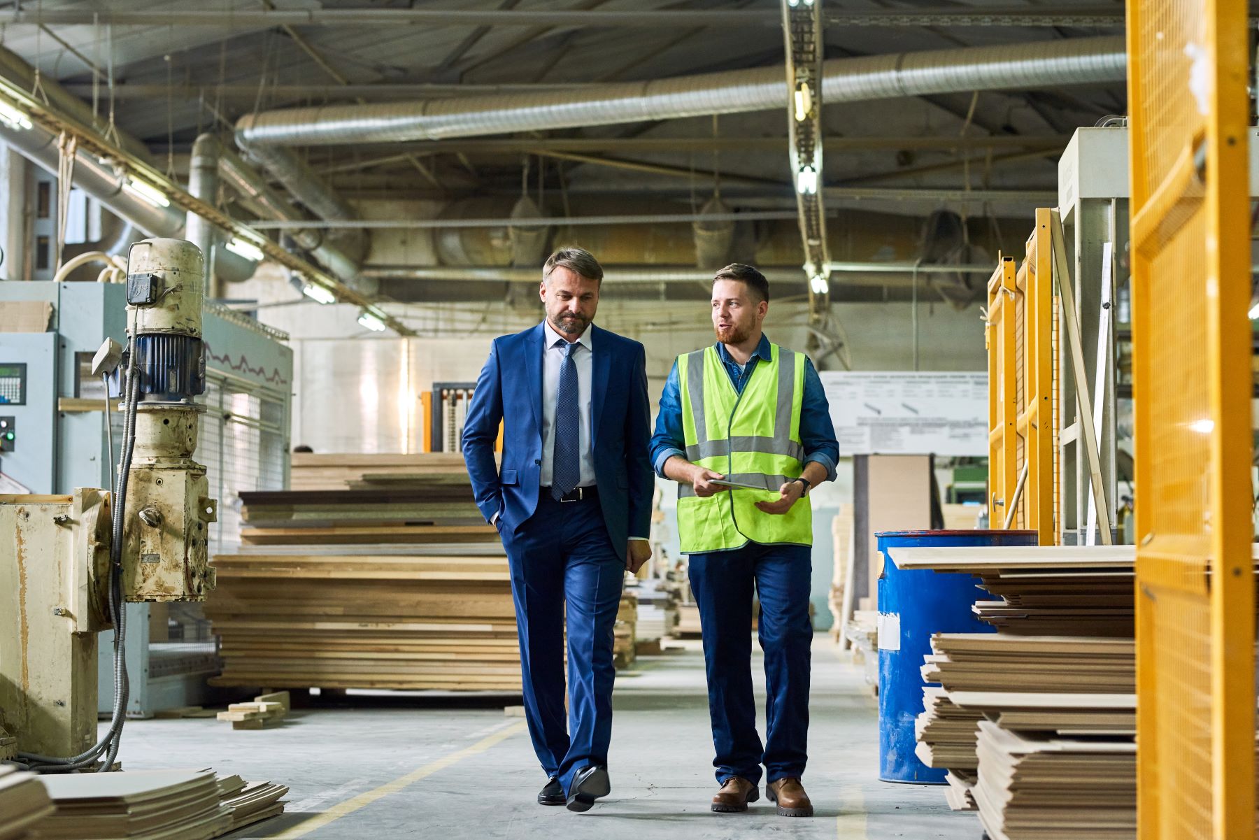 Man in suit walking through warehouse next to man in reflective vest