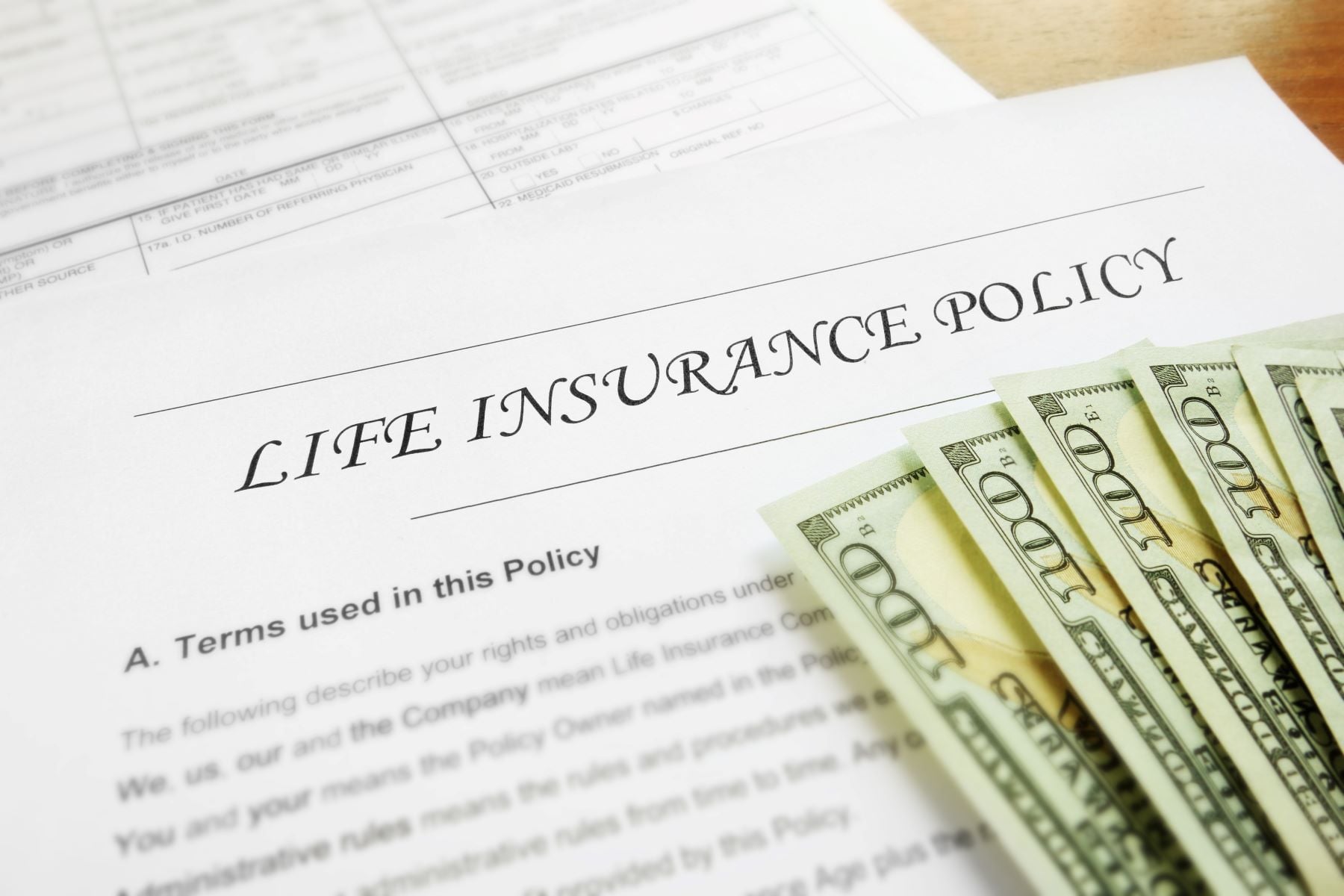 Life insurance policy paper with $100 bills stacked on top