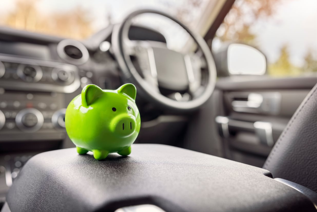 A small green piggy bank on a car seat, showing money savings