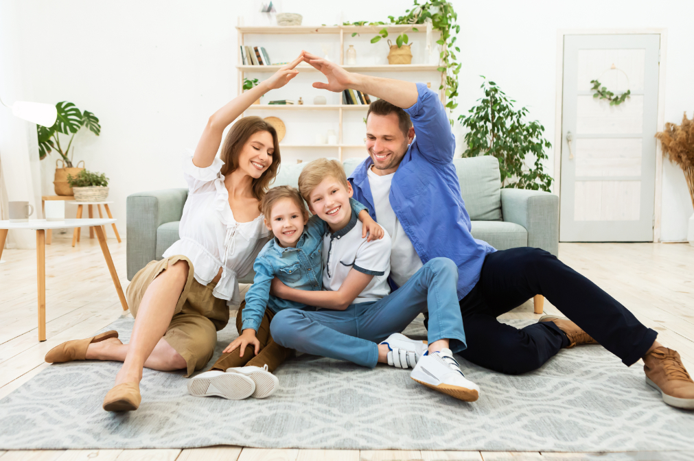 A mother and father reach their arms above their small children to make a house shape, showing that they are protected by protective life insurance