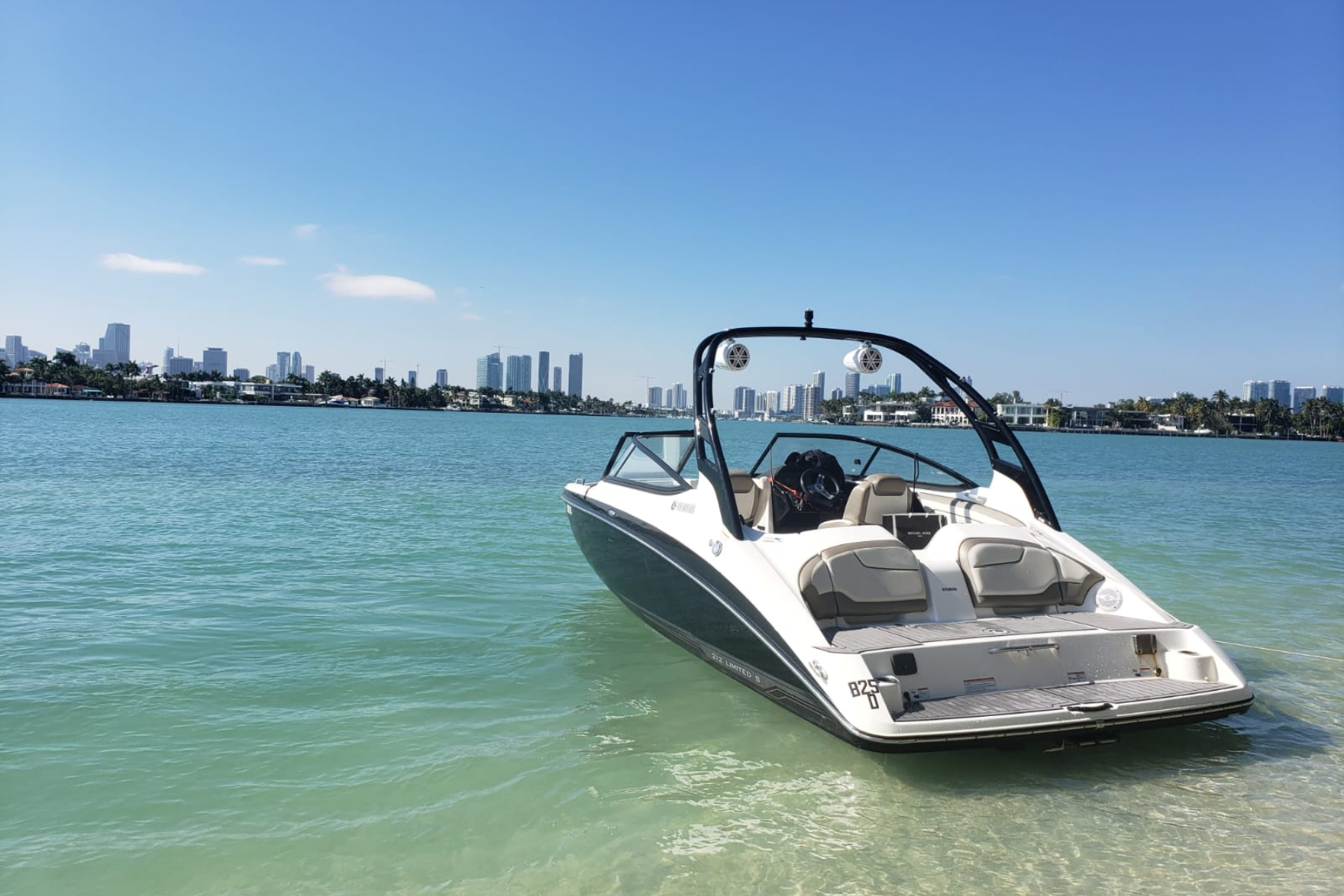 Modern white and black motorboat anchored in clear turquoise water with a city skyline in the background under a bright blue sky