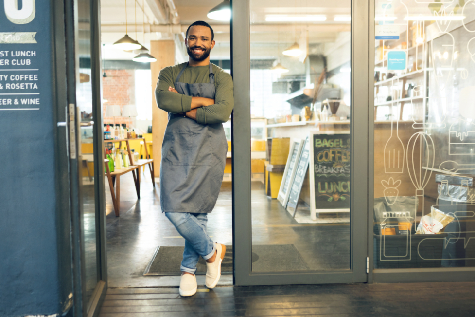 Man wearing apron while standing on door of coffee shop