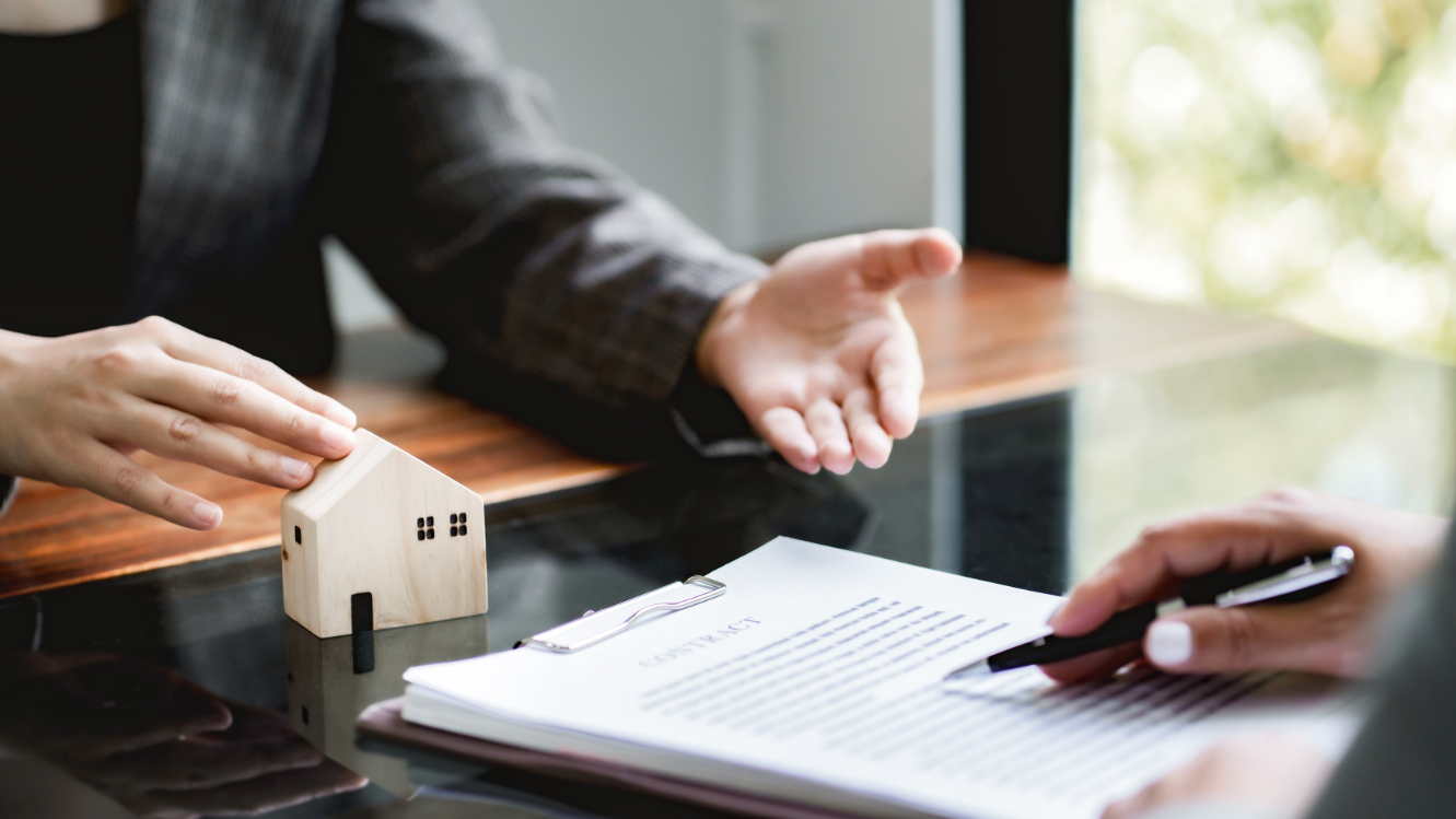 Person pointing at paper in table with small toy house