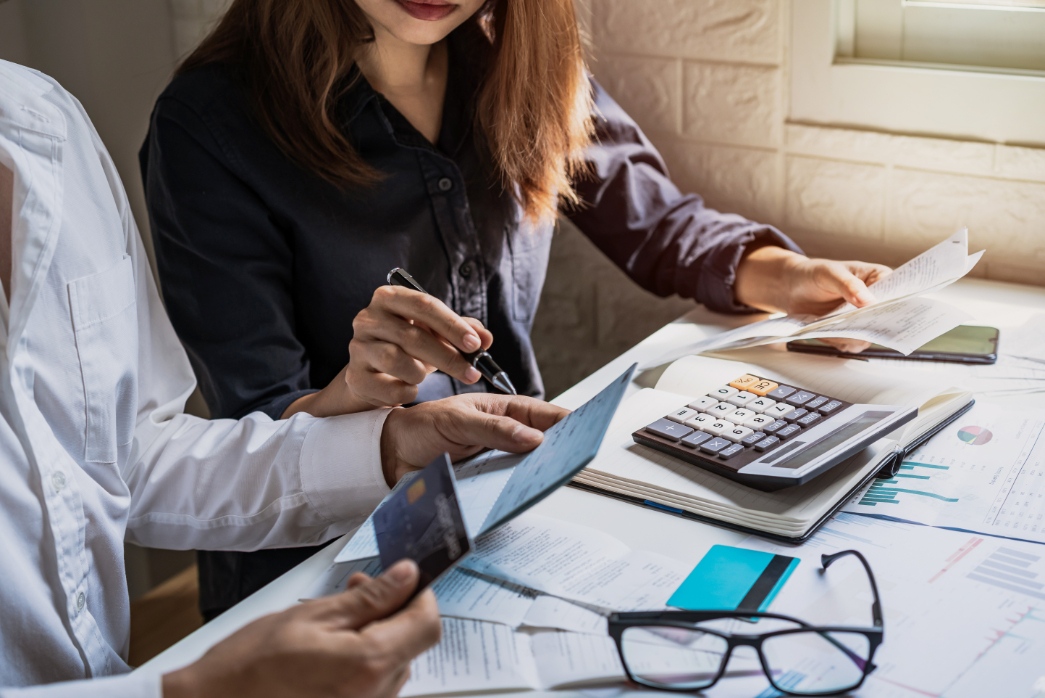 Man and women sitting on table with calculator and papers.