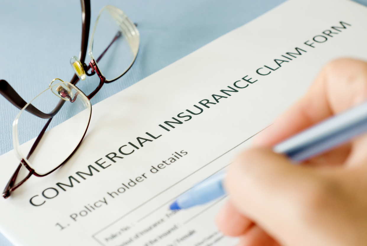 Person filling commercial insurance form in table with glasses next to it