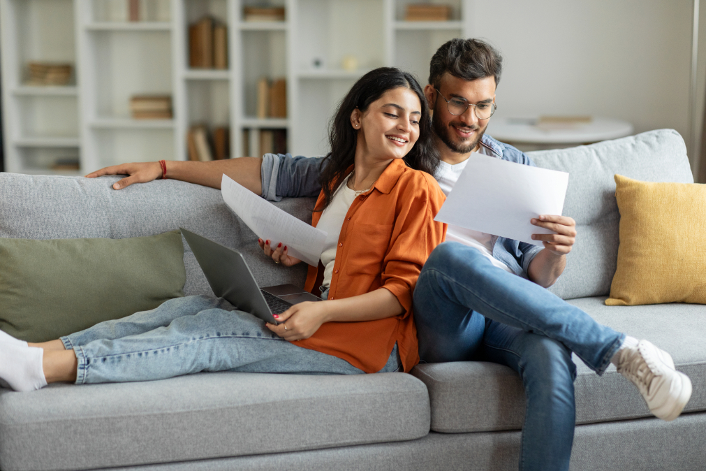 Man and woman sitting next to each other on couch holding paper in hand in living room