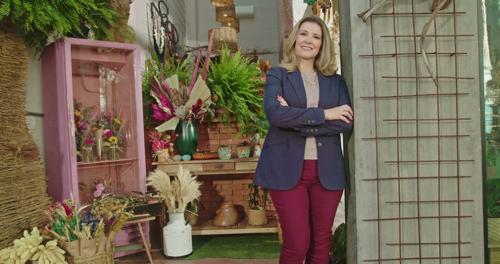 Woman crossing her arms and smilng is leaning on door frame in front of plant shop