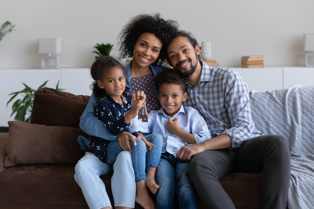 Family of four is sitting in couch, smiling and hugging.