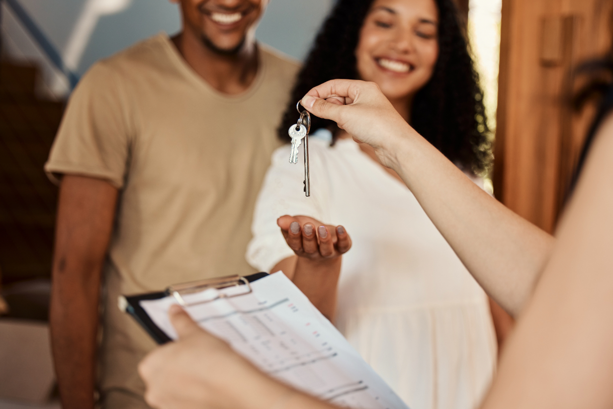 Person holding clipboard is handing keys to couple.