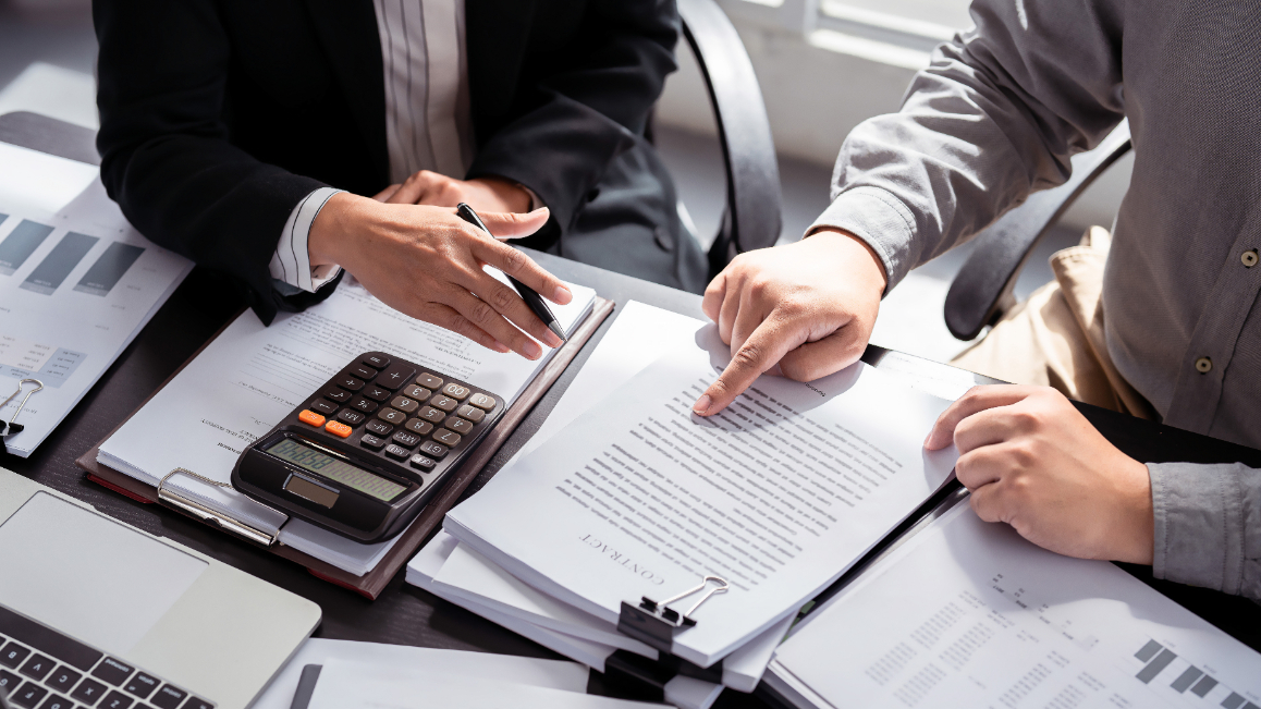 Men sitting down while discussing documents on table,with calculator.