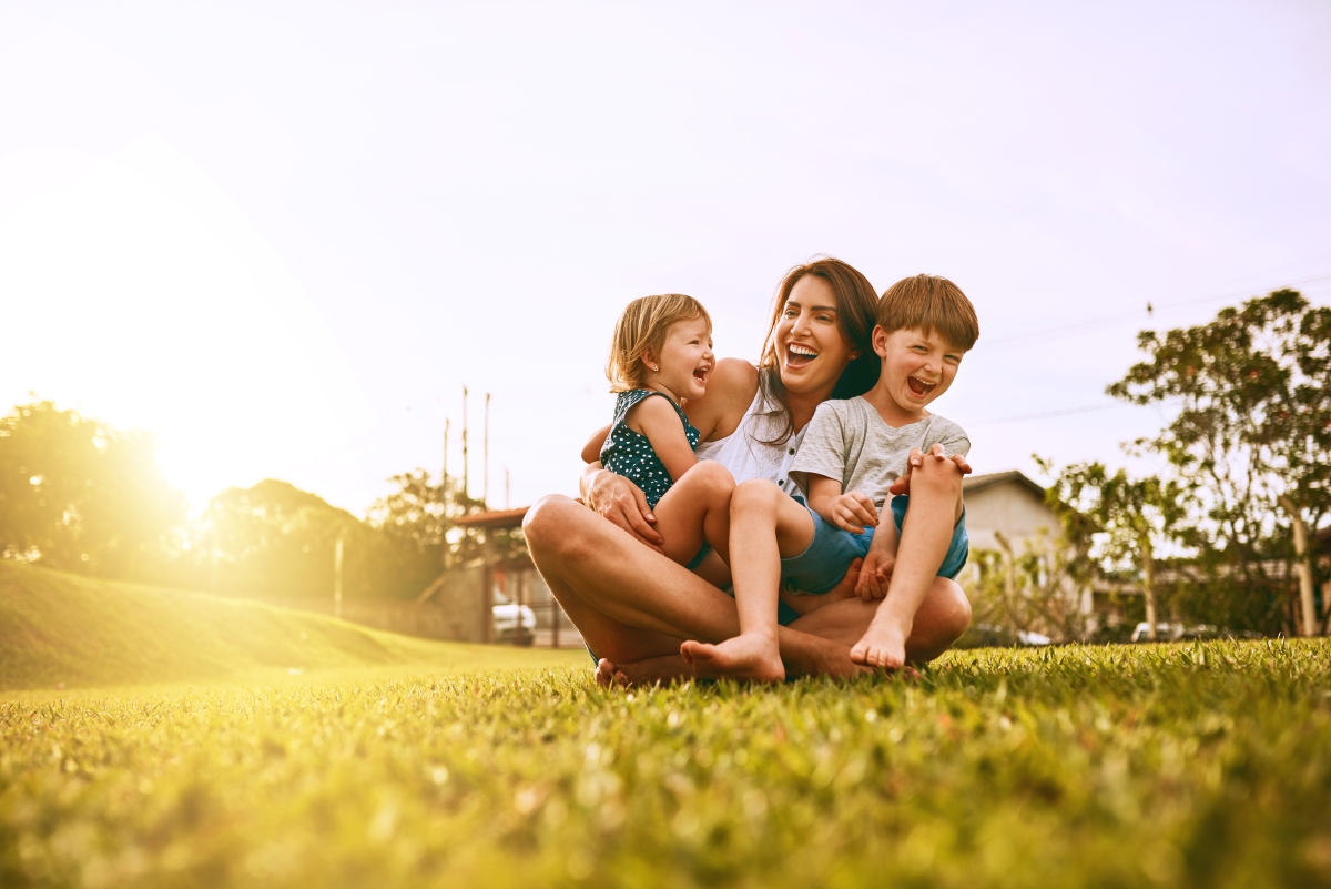 Woman and three kids hugging and smiling while sitting on yard.