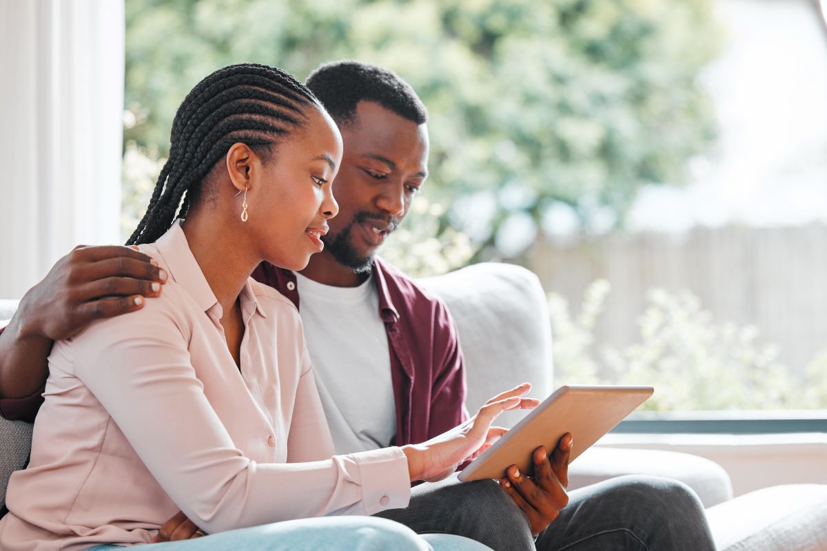 Man and woman hugging and sitting on couch while looking at tablet.