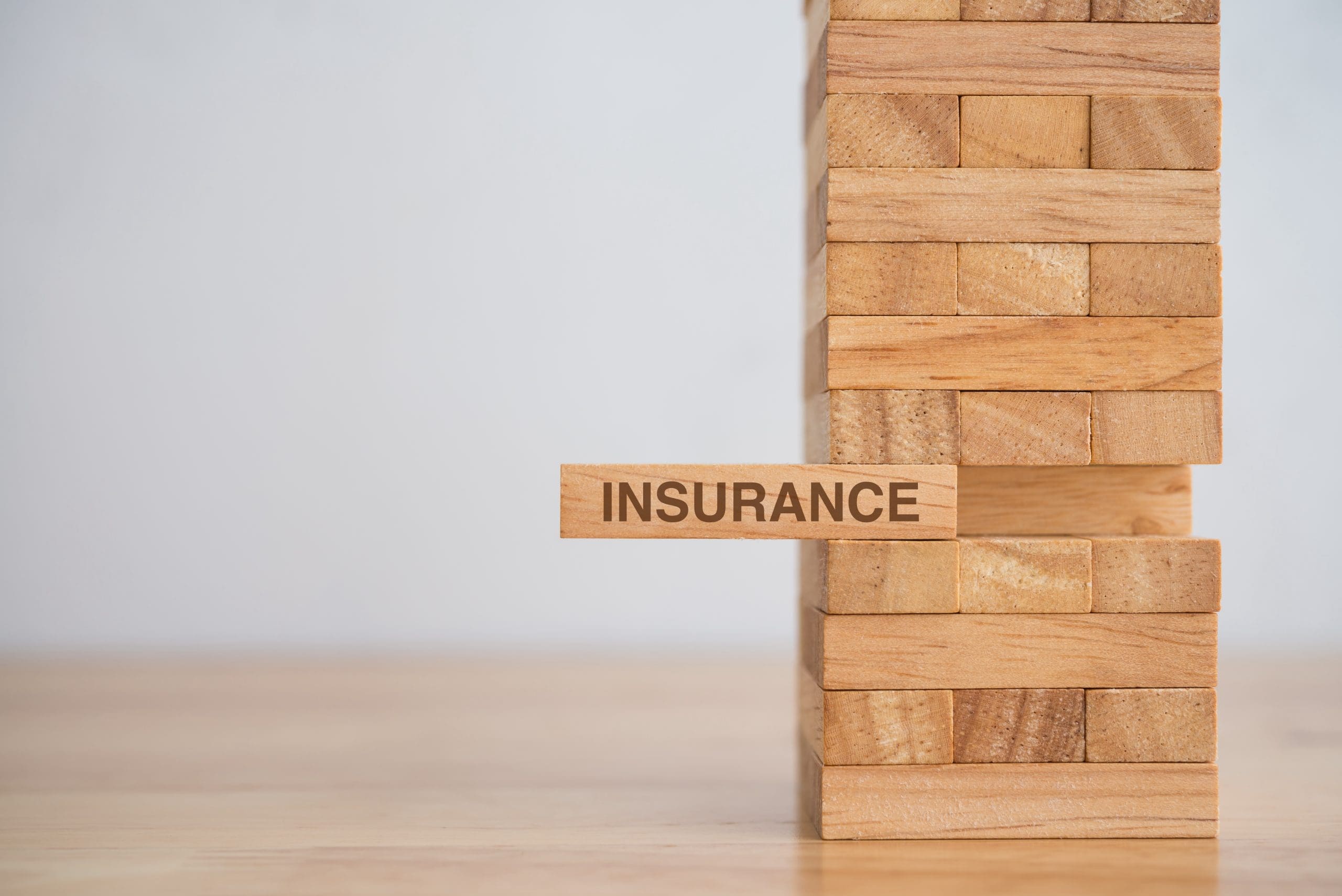 Wooden block tower stacking game with word INSURANCE on wooden table background.