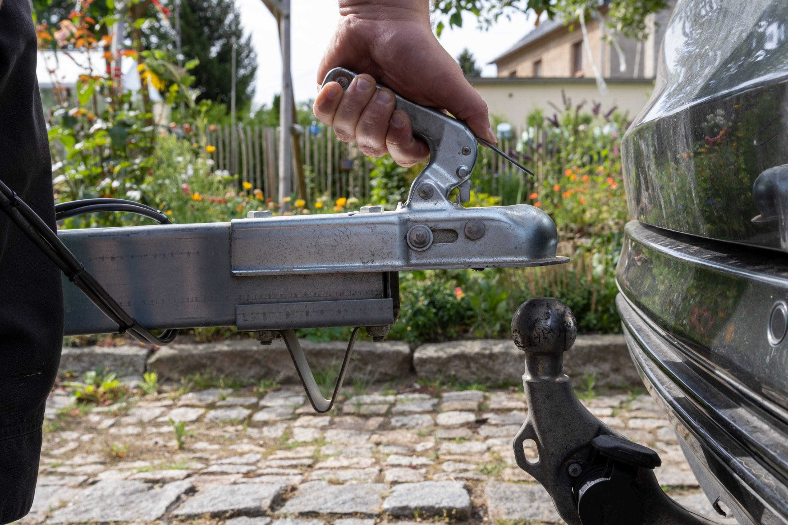 Man's hand checks the fixation of the trailer closed hitch lock handle on the towing ball towbar of the car closeup