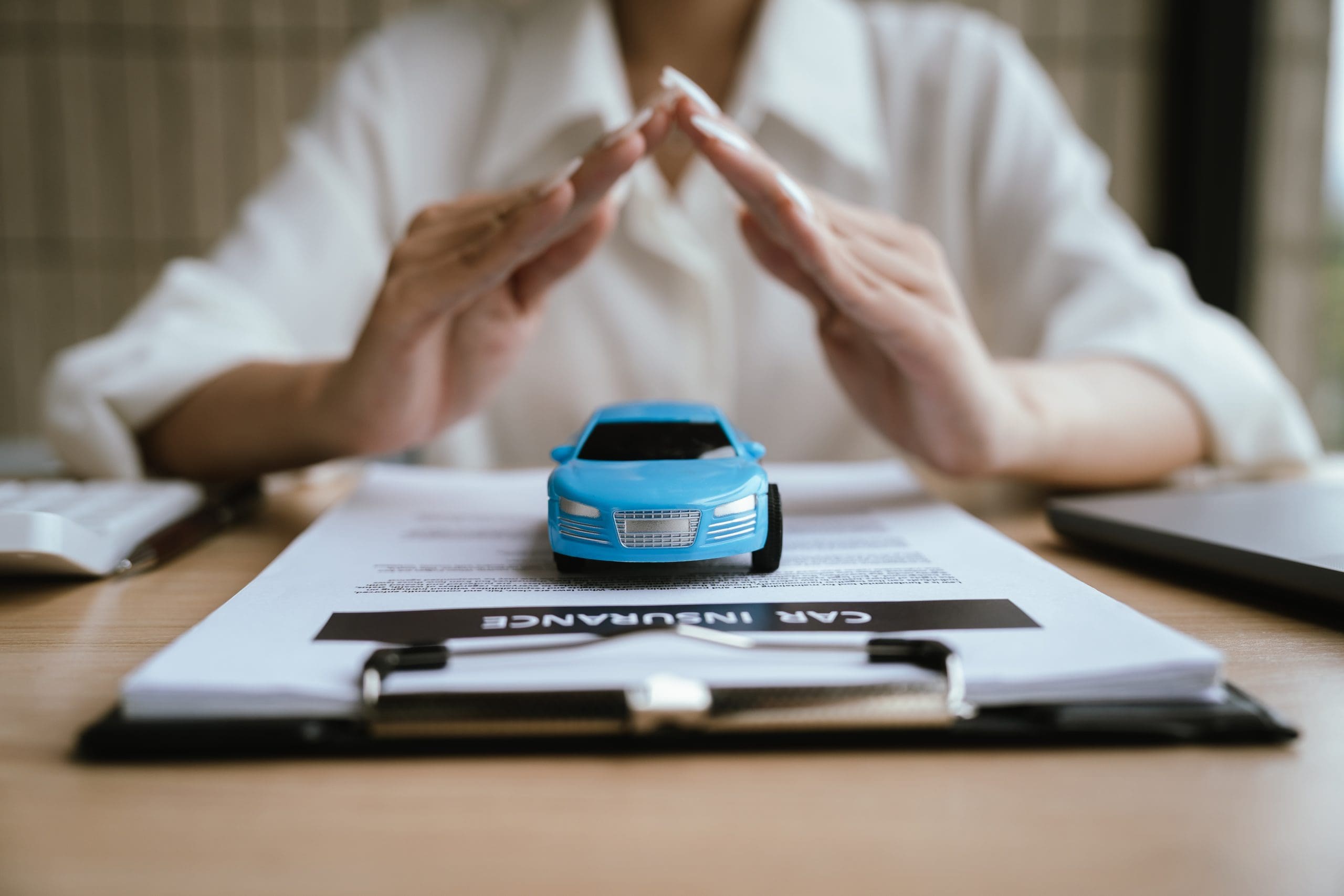 Hands protect toy car over clipboard with words car insurance.