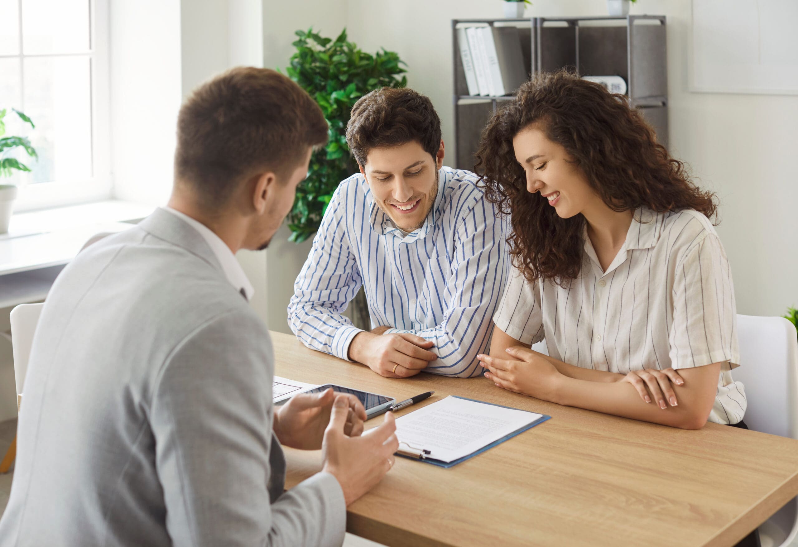 Young couple sitting in desk across from salesman showing them paperwork. Concept of couple purchasing insurance.