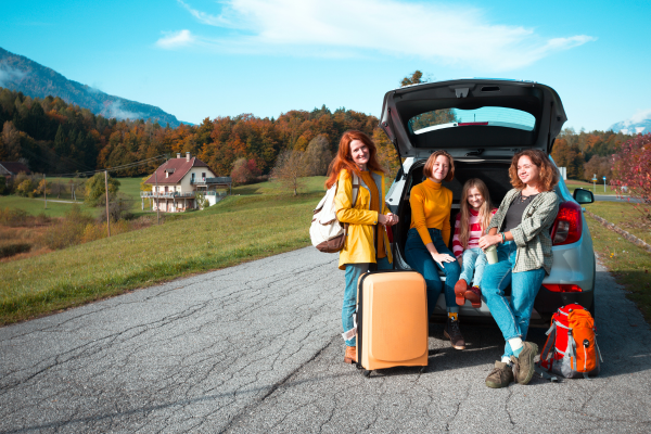 Family standing next to the back of the car, with the door open. Car parked in the middle of the road on rural setting.